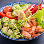 Healthy grilled salmon, avocado, tomato, cucumber, paprika and chia seeds. Balanced lunch in blue bowl. Buddha bowl.